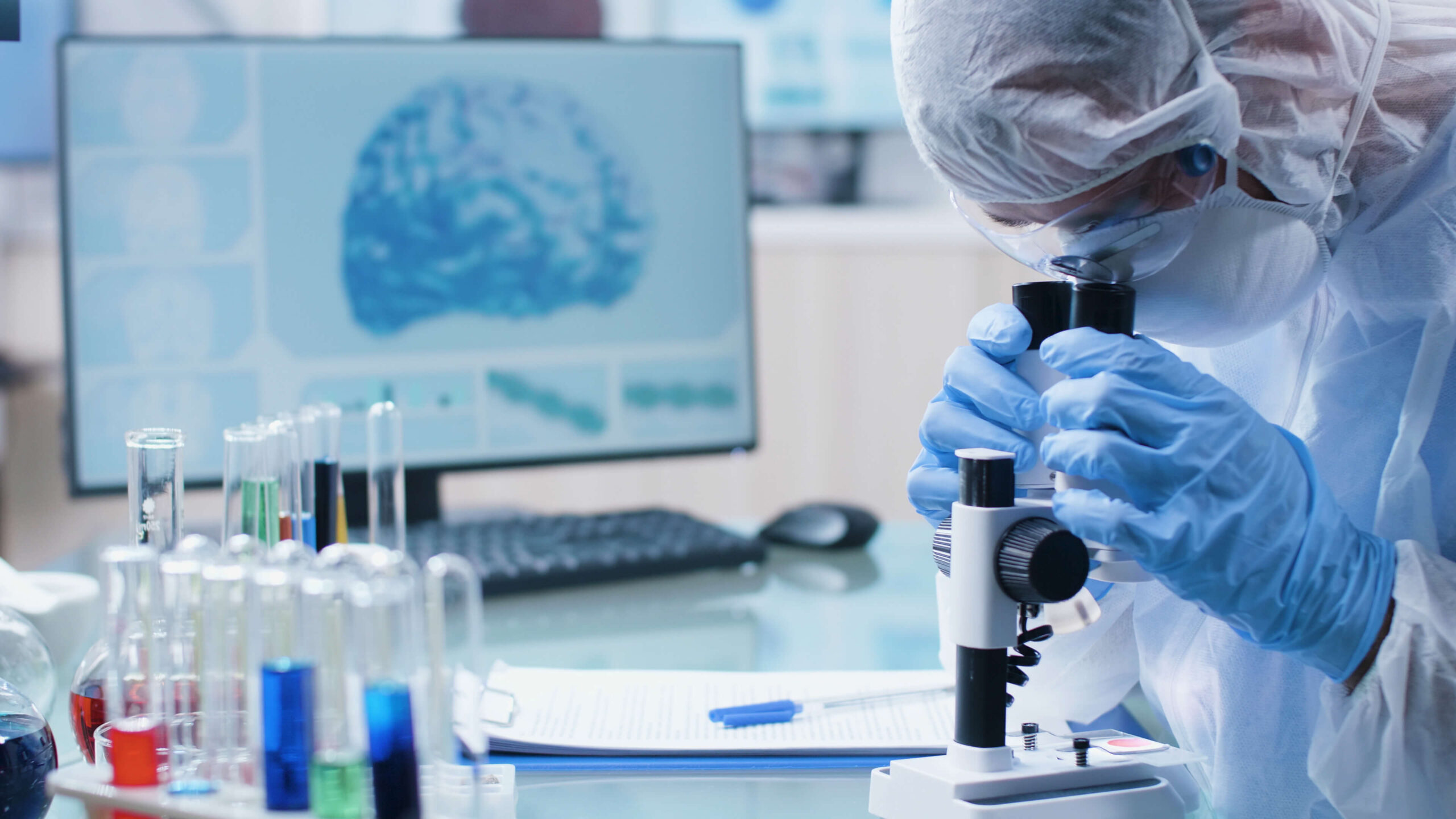 preclincal workstation with test tubes and a scientist looking at a sample through a microscope