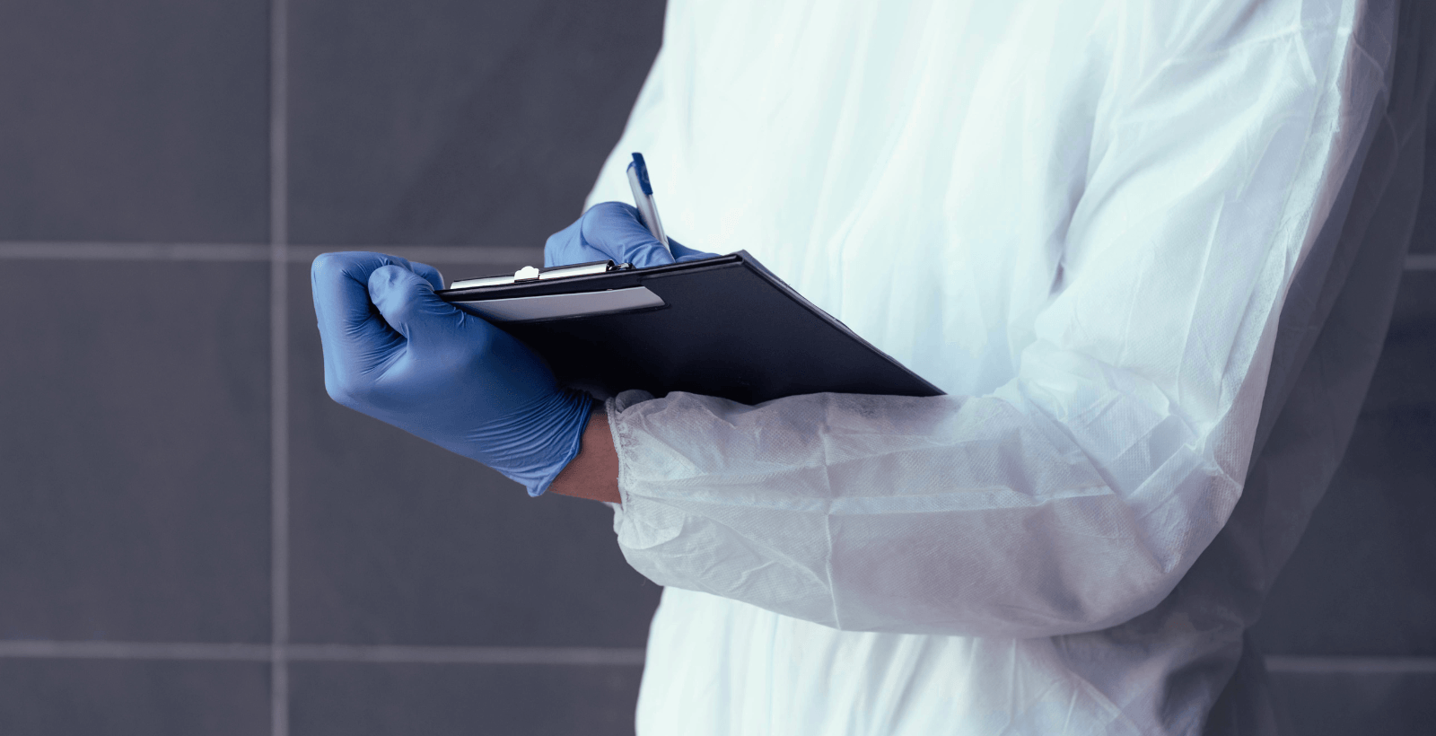 Person in lab equipment holding a clipboard and writing