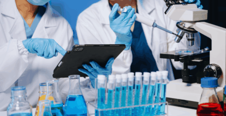 Two scientists sitting in front of a desk with research tools studying a table while performing tests using a microscope